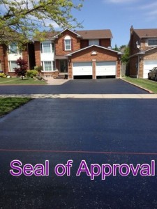 A freshly sealed asphalt driveway leading up to a two-story house with two open garage doors